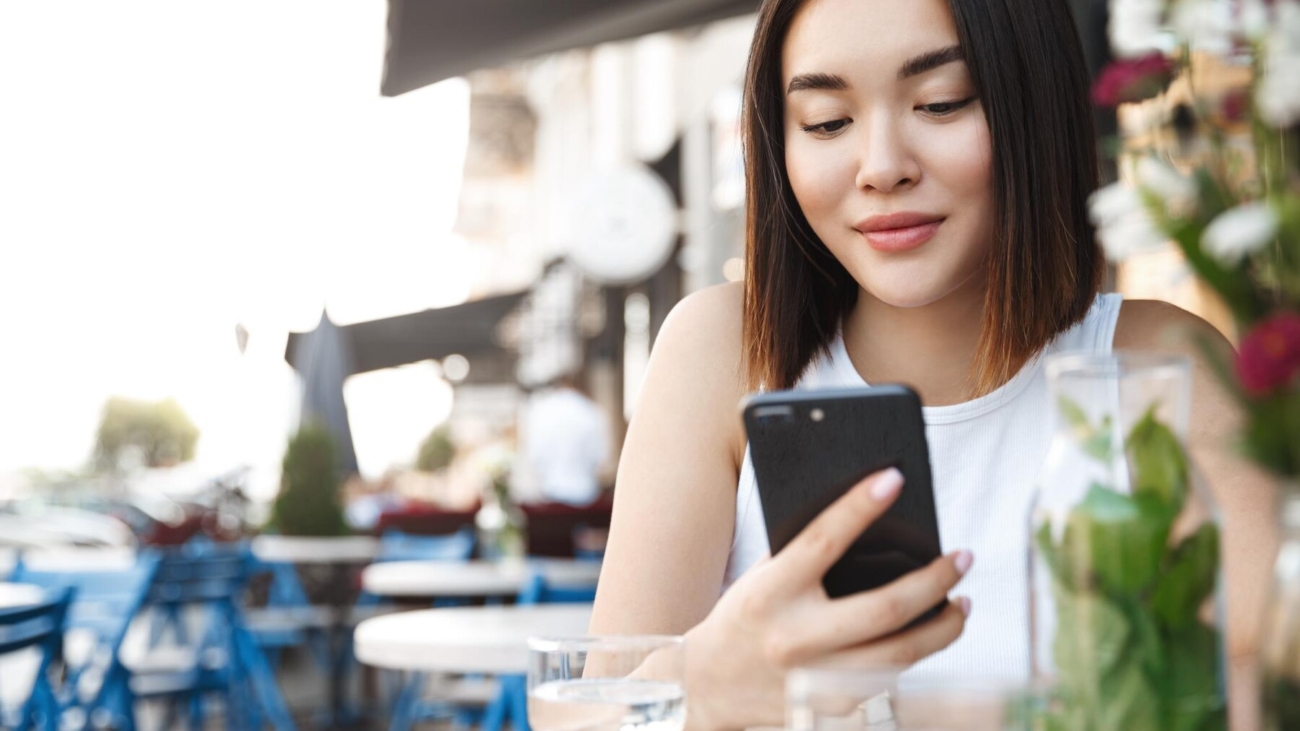 closeup-modern-asian-woman-sitting-sidewalk-cafe-with-mobile-phone-girl-reading-text-message-smartphone-while-relaxing-city_197531-30336